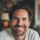 Homme souriant avec barbe et cheveux bouclés.